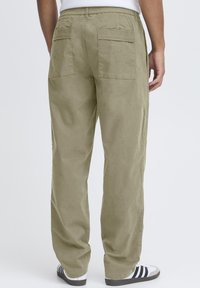 Pantalon vert olive clair en tissu doux, doté d'une ceinture élastique et de deux poches arrière. Coupe droite avec une coupe décontractée.
