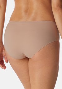 Beige hipster-pikkushousut, jotka on valmistettu sileästä ja joustavasta kankaasta, matalavyötäröinen muotoilu ja huomaamattomat saumat saumattoman ilmeen saavuttamiseksi.