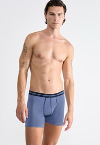 Boxers azules para hombre con una cinturilla elástica negra que presenta el logo de la marca, tejido suave y un ajuste ceñido con una parte delantera definida.