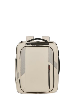 Quadratischer Rucksack in Cremefarbe mit schwarzen Reißverschlüssen, Mesh-Akzenten, Tragegriff oben und gepolsterten Schultergurten vor weißem Hintergrund.