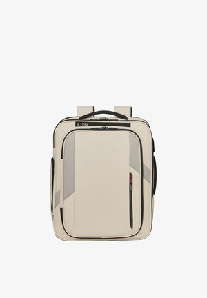 Cream-colored square backpack with black zippers, mesh accents, top handle, and padded shoulder straps shown against a white background.