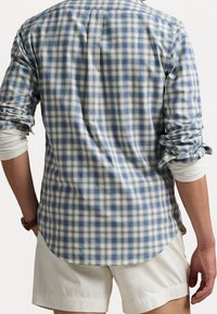 Sininen ja kerma ruudullinen paita pitkillä hihoilla, nappikauluksella ja kaarrettulla helmalla; käytetään valkoisen pitkähihasen paidan päällä, näytetään takaa.