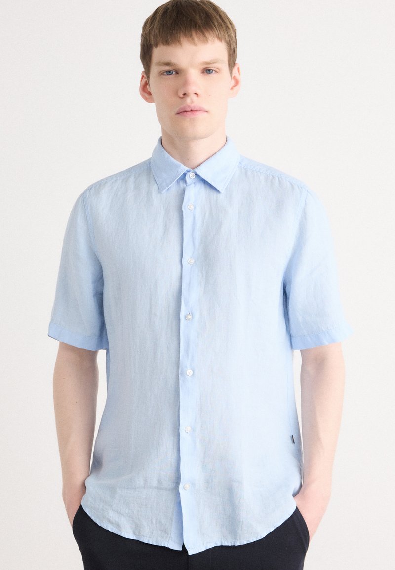 Light blue short-sleeve shirt with a button-down collar, made of textured fabric, featuring a straight hem and white buttons.