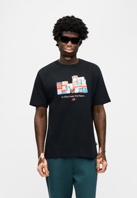 Μαύρο βαμβακερό μπλουζάκι με γραφικό στοιχείο από στοιβαγμένα κουτιά παπουτσιών. Κοντά μανίκια, στρογγυλή λαιμόκοψη και άνετη γραμμή. Συνδυάζεται με τιρκουάζ παντελόνια.