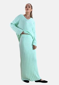 Mintgrøn, ribstrikket top og matchende lang nederdel. Stoffet er blødt og tekstureret. Outfitet har vide ærmer og en afslappet pasform.