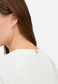 Witte blouse met een ronde halslijn, voorzien van een contrasterende gestreepte accent aan de achterkant. Zachte textuur en schoon ontwerp zijn duidelijk zichtbaar.