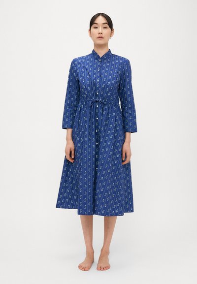 Blauwe jurk met een knoopsluiting aan de voorkant, lange mouwen en een geraffineerde taille. Heeft een herhalend patroon in wit en groen. Gladde stof, midi-lengte.