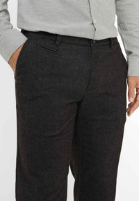 Pantaloni grigi scuri realizzati in tessuto testurizzato, con una vestibilità dritta, tasche laterali e una linea frontale piatta. Adatti per un abbigliamento casual o formale.