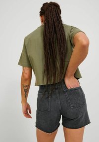 Top corto oliva y pantalones cortos de mezclilla negros de talle alto. Los pantalones cortos tienen un dobladillo deshilachado y dos bolsillos traseros. El cabello está peinado en largas trenzas.