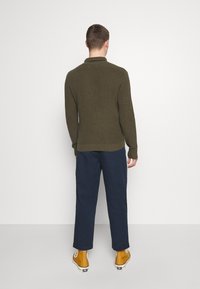 Olivgrön ribbad tröja, åtsittande siluett, långa ärmar, kombinerad med marinblå vida byxor och gula hög-hals sneakers.