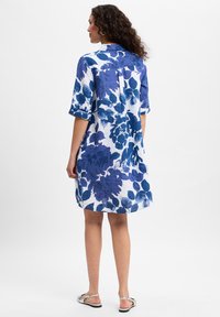 Floral dress featuring a blue and white pattern, short rolled sleeves, and a buttoned back. Made from lightweight fabric. Mid-thigh length.