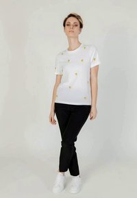 T-shirt de algodão branca com bordado de limão amarelo, gola redonda, mangas curtas, combinada com calças pretas e ténis brancos. Design minimalista.