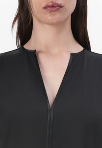 Black garment with a deep V-neckline, featuring a smooth texture and slim fit. Accented with a subtle seam detail along the neckline.