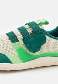 Lekkie sneakersy z beżową siateczkową cholewką, zielonymi akcentami z gumy i trzema ciemnozielonymi paskami dla pewnego dopasowania. Teksturowana podeszwa zapewniająca przyczepność.