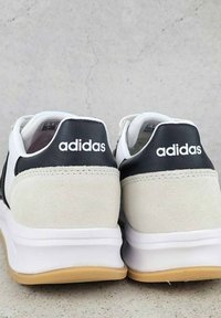 Des baskets Adidas blanches et noires présentent un dessus en suède et en cuir, avec une semelle en caoutchouc et le nom de la marque affiché sur le talon.