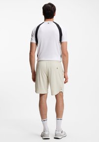 Fehér sportpóló fekete részletekkel és rövid ujjakkal, világos bézs rövidnadrággal párosítva. Hátul logóval és csíkos díszítéssel ellátva.