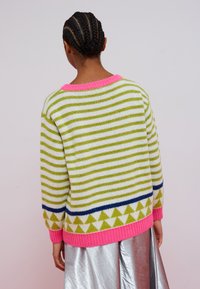 Stribet striktrøje i grøn, hvid og blå med en pink krave og kant. Har trekantmønstre i bunden og lange ærmer.