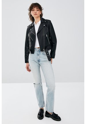 Zwart leren motorjack met zilveren ritsen, gecombineerd met lichtblauwe distressed jeans en zwarte schoenen. Gladde textuur, klassiek ontwerp.