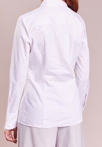 Camicia bianca a maniche lunghe con un design aderente, texture sottile e colletto classico. Presenta spacchetti laterali e polsini con bottone.