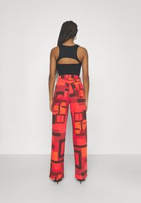 Top preto sem mangas com costas abertas; calças largas em vermelho e laranja com padrões geométricos e acentos escuros contrastantes.