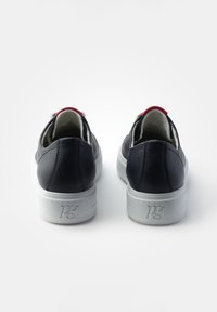 Baskets en cuir noir avec semelles blanches, présentant un accent rouge au talon et une finition texturée. Logo visible sur la semelle.