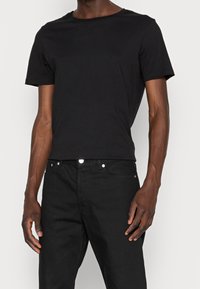 Black cotton T-shirt with a crew neckline and short sleeves, paired with dark denim jeans featuring silver button accents.
