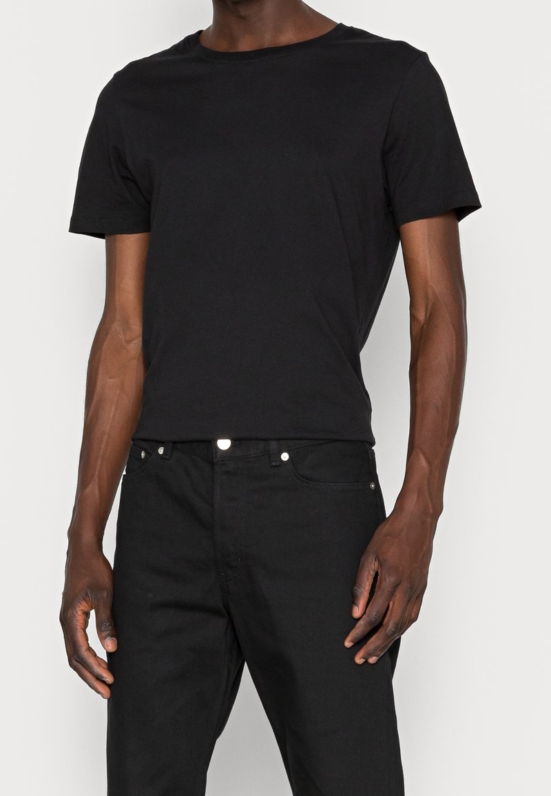 Black cotton T-shirt with a crew neckline and short sleeves, paired with dark denim jeans featuring silver button accents.