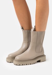 Botines beige hasta el tobillo con un acabado de cuero suave, paneles laterales elásticos, lengüetas de agarre y suelas de goma con diseño para mayor tracción.