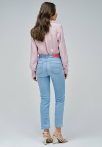 Jeans de color azul claro con una cintura alta, diseño ajustado y bolsillos traseros. Combinados con una camiseta de manga larga rosa y sandalias con tiras.