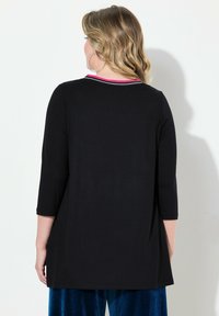 Svart tunika med trekvartslånga ärmar och avslappnad passform. Har en rund halsringning med kontrasterande rosa och vit kant. Slät textur.