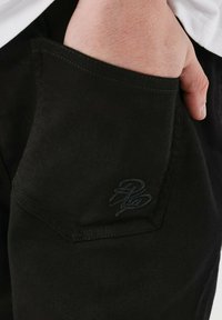 Sorte bomuldsbukser med en sidelomme med et diskret broderet logo, struktureret design og glat tekstur.