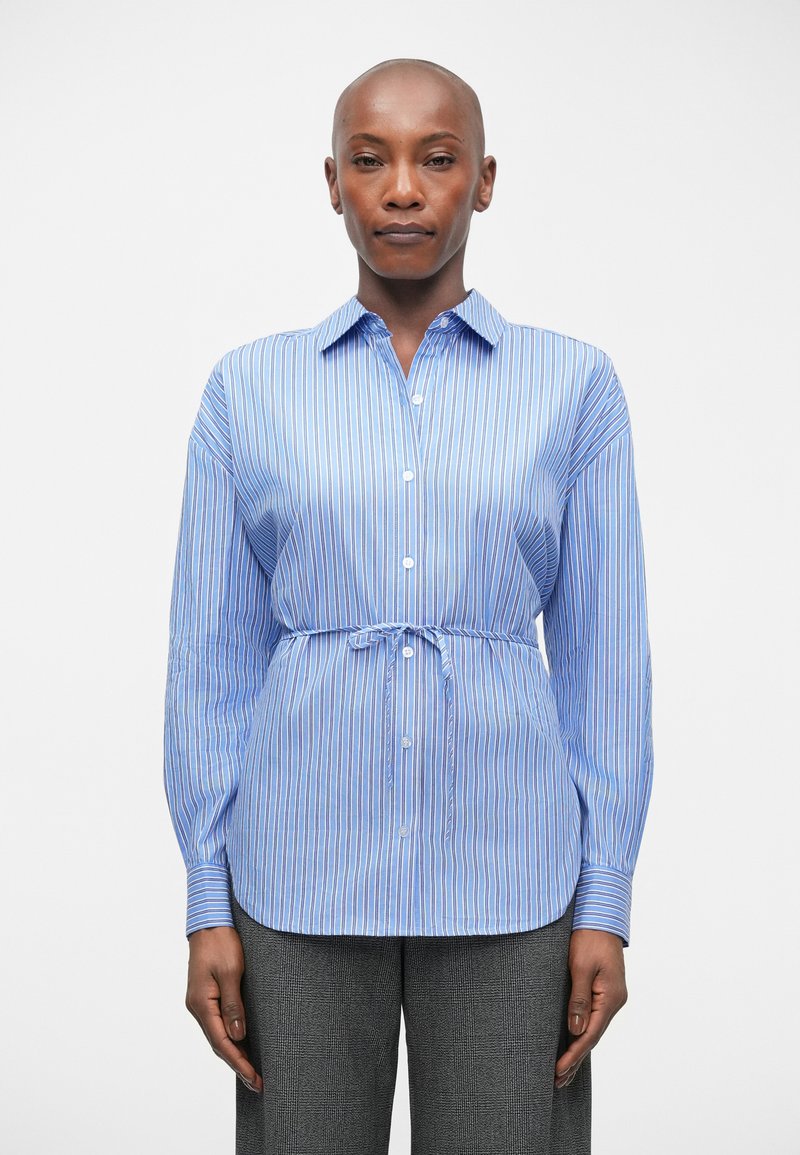 Lichtblauw gestreept shirt met een knoopsluiting aan de voorkant, lange mouwen en een strikaccent op de taille. Zachte stof met een gladde, ademende textuur.