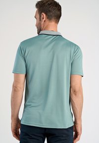 Polo a maniche corte di colore verde menta con colletto grigio a contrasto. Texture liscia, spacco laterale all'orlo e vestibilità rilassata.