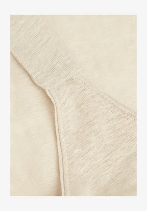 Beige stickad plagg med en mjuk textur, som har en bred axelrem och subtila variationer i trådtjocklek.