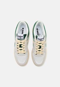White leather sneakers with green suede accents, flat beige laces, textured rubber sole, perforated toe, and logoed insoles.