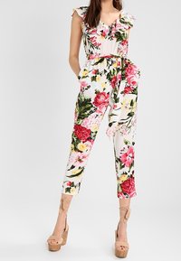 Floral jumpsuit with ruffled shoulders, featuring pink and red flowers on a white background, tied waist, and fitted ankle-length legs.