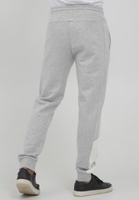 Graue Jogginghosen mit tailliertem Design, elastischem Bund, Seitentaschen und einem kontrastierenden weißen Einsatz entlang des Unterschenkels. Getragen mit schwarzen Sneakers.