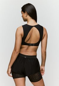 Sujetador deportivo negro con corte en la espalda y cierre ajustable, combinado con pantalones cortos negros que presentan un patrón de encaje en la mitad inferior.