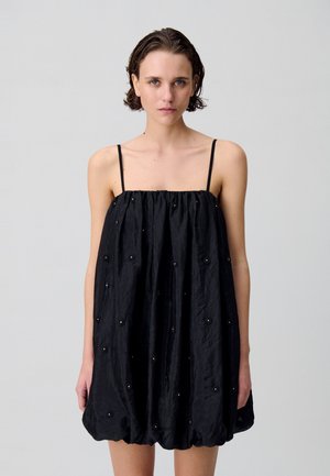 Abito nero senza maniche con una vestibilità comoda, caratterizzato da un tessuto testurizzato e dettagli in perline lungo tutto il design.