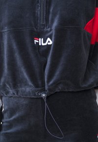 Zwarte fleece hoodie met een halve rits, rode accenten en een wit geborduurd logo. Voorzien van een verstelbare trekkoord aan de zoom.