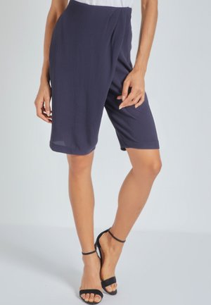 Bermudas azul marino hechas de un tejido ligero, con un corte relajado y a la altura de la rodilla, y una sutil textura, combinadas con sandalias negras.