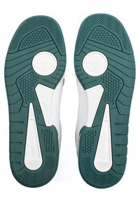 Bijele tenisice s teksturiranom zelenom gumom potplatom. Potplat ima uzorke za grip i kružne akcentne detalje, dizajnirane za neklizajuće površine.
