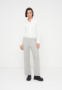 Chemise blanche à boutons avec col, associée à un pantalon en maille côtelée gris clair, à jambes larges et taille élastique. Bottes noires épaisses.