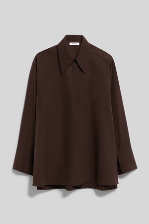 Camicia marrone scuro a maniche lunghe con colletto ampio e maniche con polsini, appesa su uno sfondo grigio chiaro uniforme.
