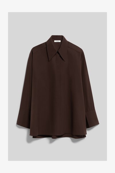 Chemise marron foncé à manches longues avec large col et manches à revers, suspendue sur un fond uni gris clair.