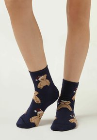 Marine ankelsokker lavet af bomuldsblanding med strikkede teddy-bear mønstre iført røde og hvide hatte, med en glat tekstur.