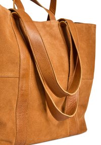 Sac fourre-tout en daim marron avec des poignées en cuir texturé, gros plan montrant les détails de couture et de matériau sur un fond blanc.