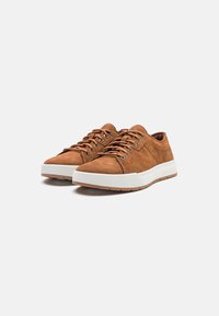 Bruna mocka sneakers med vit gummisula, runda snörningar och medelhög profil. Funktioner inkluderar sömnadsdetaljer och en slät textur.