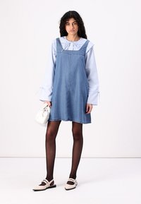 Lys blå denimkjole med firkantet hals, lagd over en blåstripet bluse. Svarte strømpebukser og beige leiligheter fullfører antrekket. Liten hvit veske.