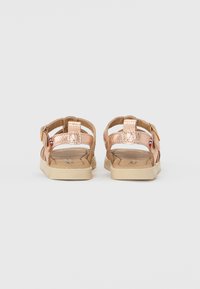 Sandales métalliques rose gold avec brides arrière, tige texturée, boucles ajustables et semelles en caoutchouc beige. Design plat avec semelles intérieures douces.